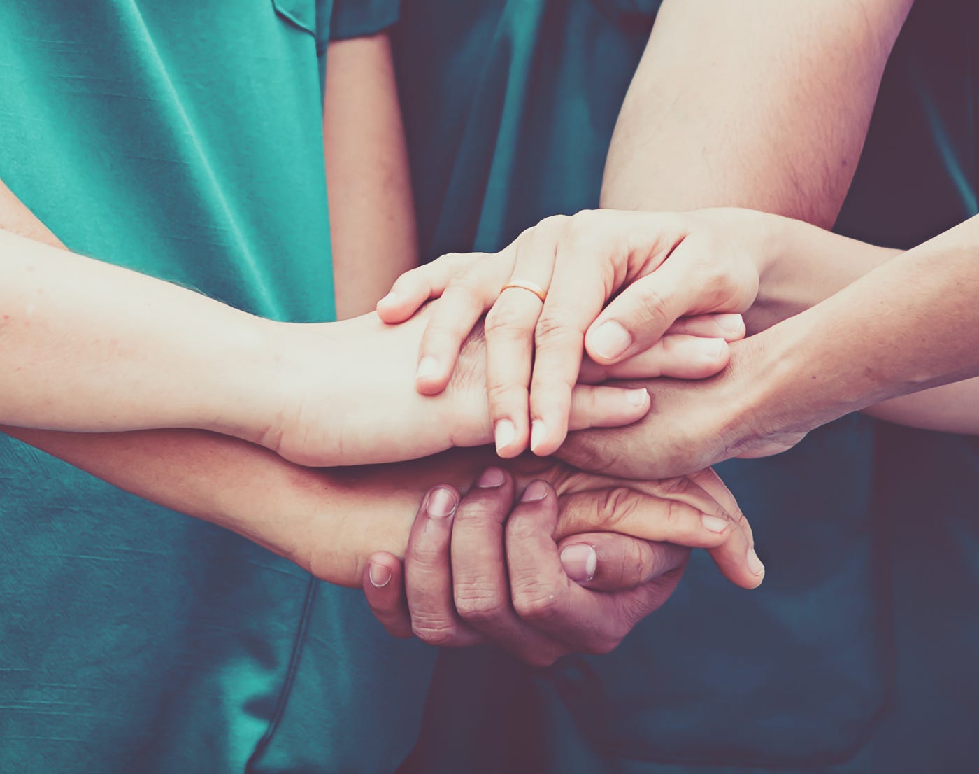 5 personas del staff vestidas con uniforme médico verde, uniendo sus manos en el centro formando un equipo multidiciplinario.